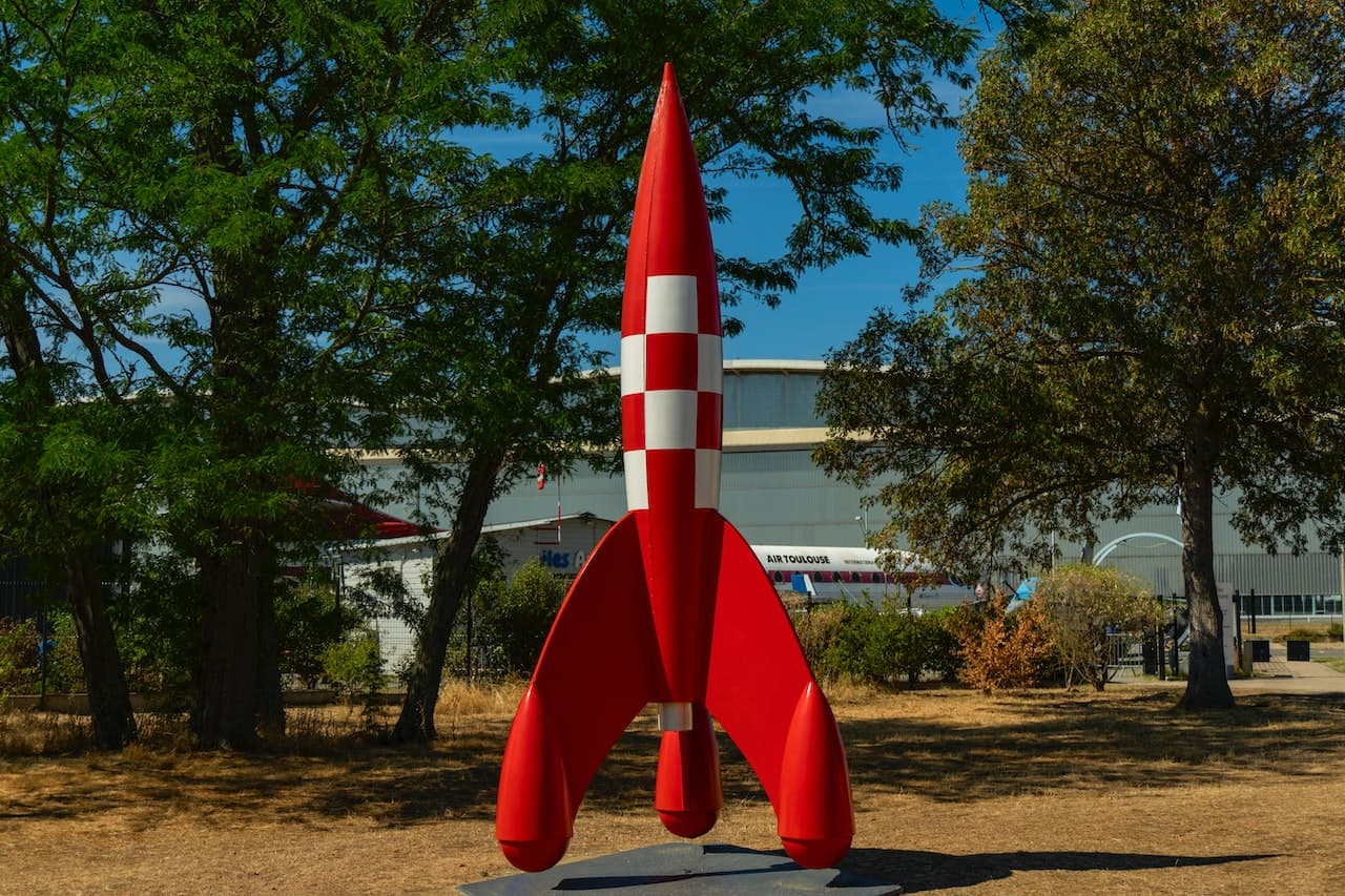 Modello di un razzo di colore rosso posto in verticale in un'area verde per esporlo. Il razzo segue molti principi della fisica cinematica quando è in volo.