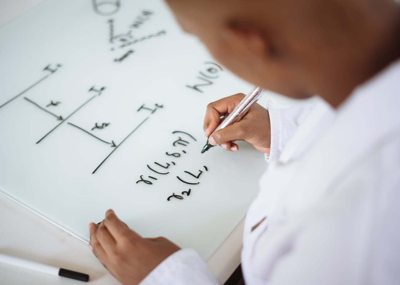 Ingegnere mentre scrive delle formule di fisica cinematica su una lavagna bianca.