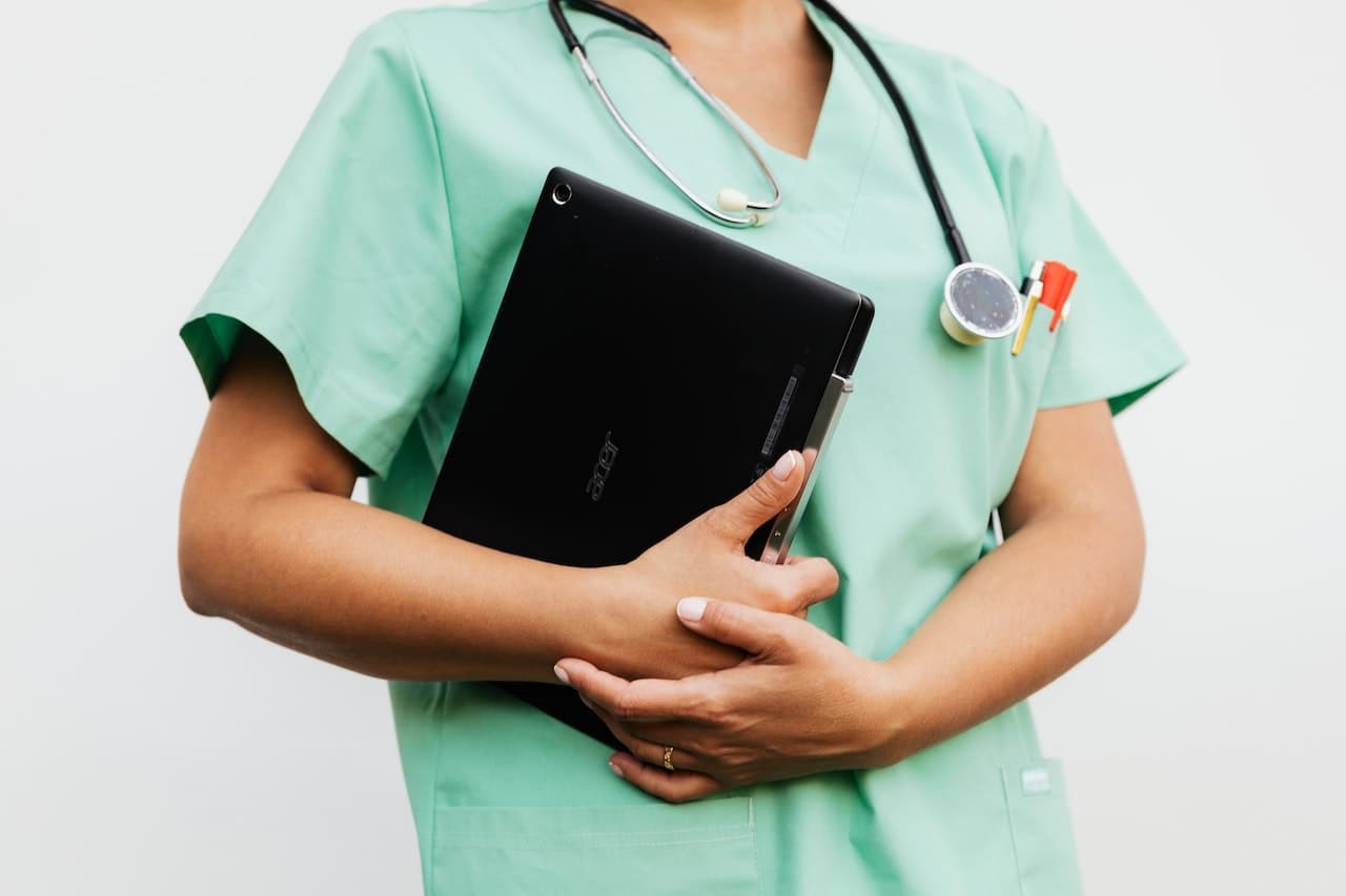 Dottoressa con indosso uno scrub verde e uno stetoscopio al collo. In mano ha un tablet.