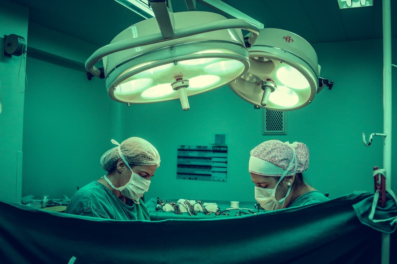 Sala operatoria co luci fredde e pareti verdi. Ci sono due neurochirurghi concentrati su un'operazione non visibile perché coperta da un telo.