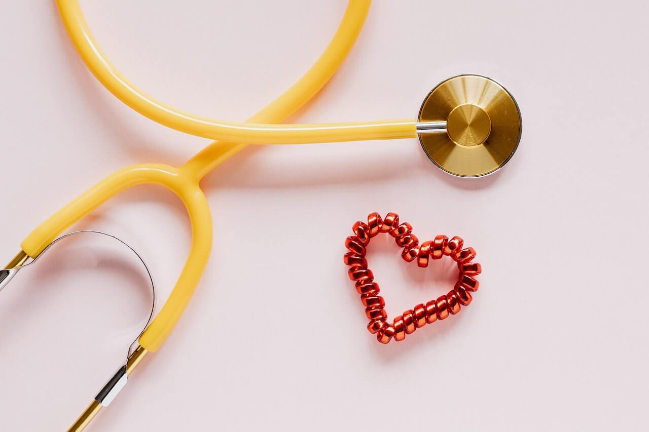 Caleidoscopio giallo e oro vicino a un nastro rosso a forma di cuore. Entrambi gli oggetti sono posti su uno sfondo rosa.