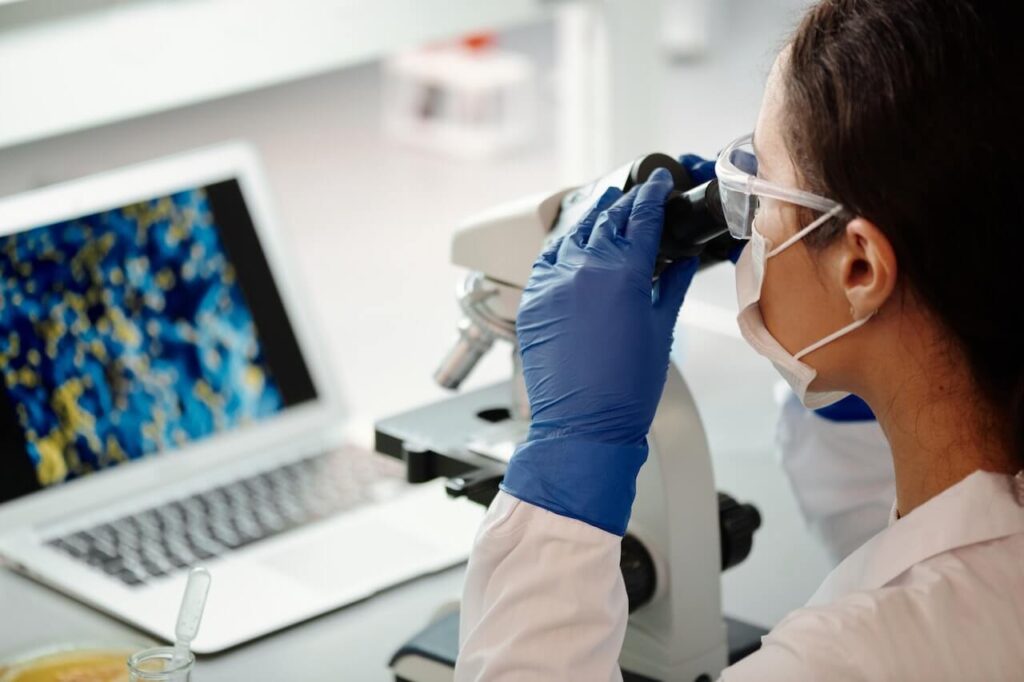 Laureata in biotecnologie mentre analizza un campione utilizzando il microscopio e il computer.