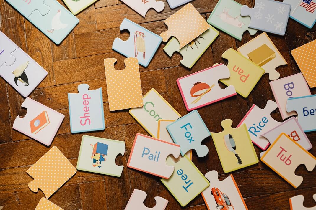 Pavimento in legno con sopra delle tessere di un puzzle con parole e disegni associati da mettere insieme.