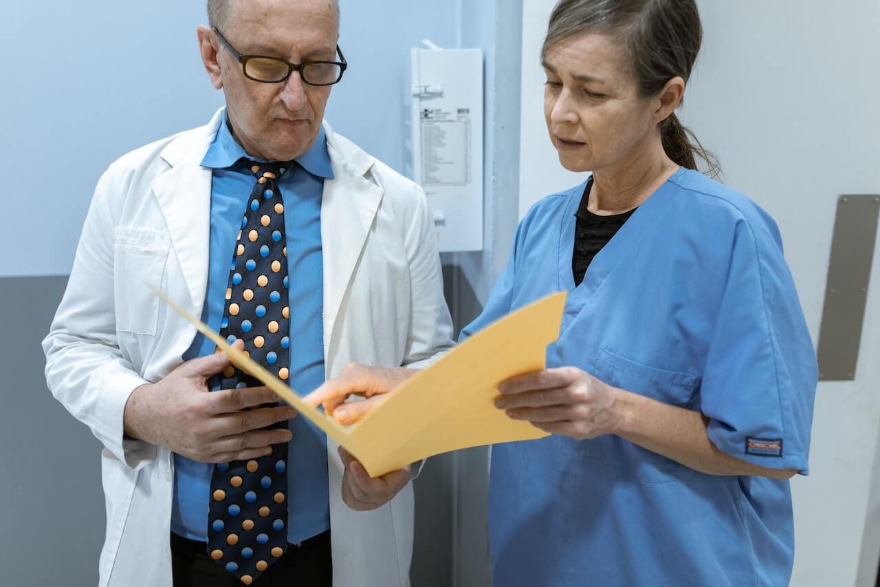 Logopedista che parola con un medico per discutere il miglior percorso terapeutico di un paziente. Guardano una cartella gialla mentre sono nel corridoio di un ospedale.