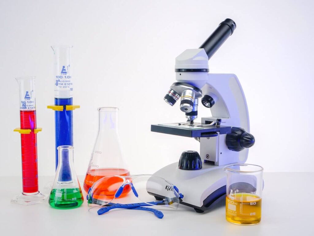Microscopio, occhiali protettivi, becker e fiale in un laboratorio per le analisi chimiche.