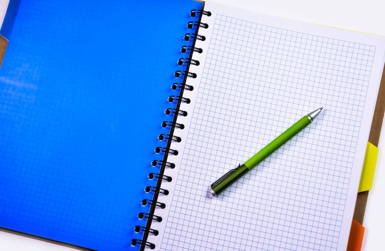 Quaderno con fogli a quadretti e una penna poggiata sulla pagina.