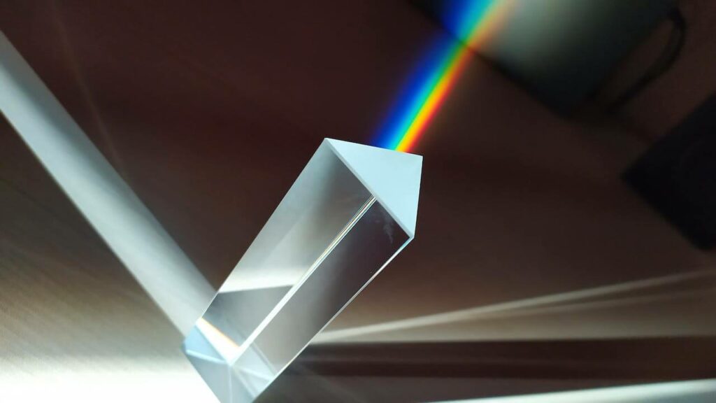 Prisma trasparente a base triangolare che riflette un raggio di luce su una parete scura. 