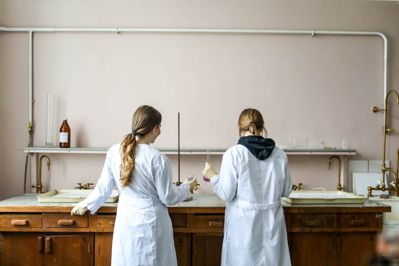 Due ragazze in un laboratorio chimico con indosso un camice bianco. Stanno lavorando con le ampolle per analizzare un fenomeno chimico.