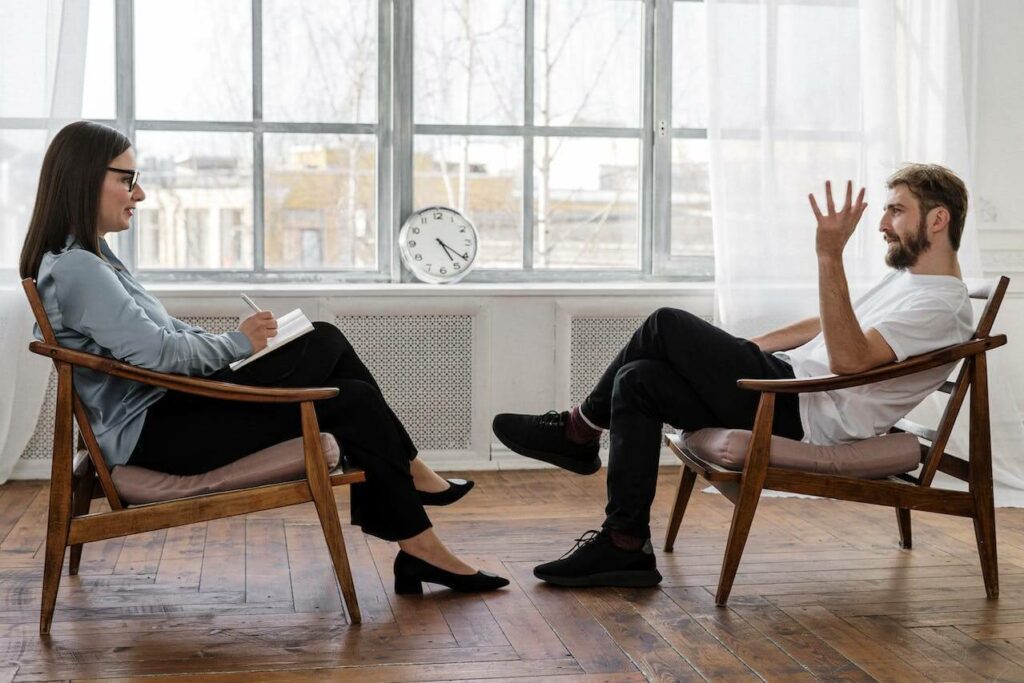 Psicoterapeuta insieme a un paziente durante una sessione di terapia in studio. I due sono seduti l'una di fronte all'altro.