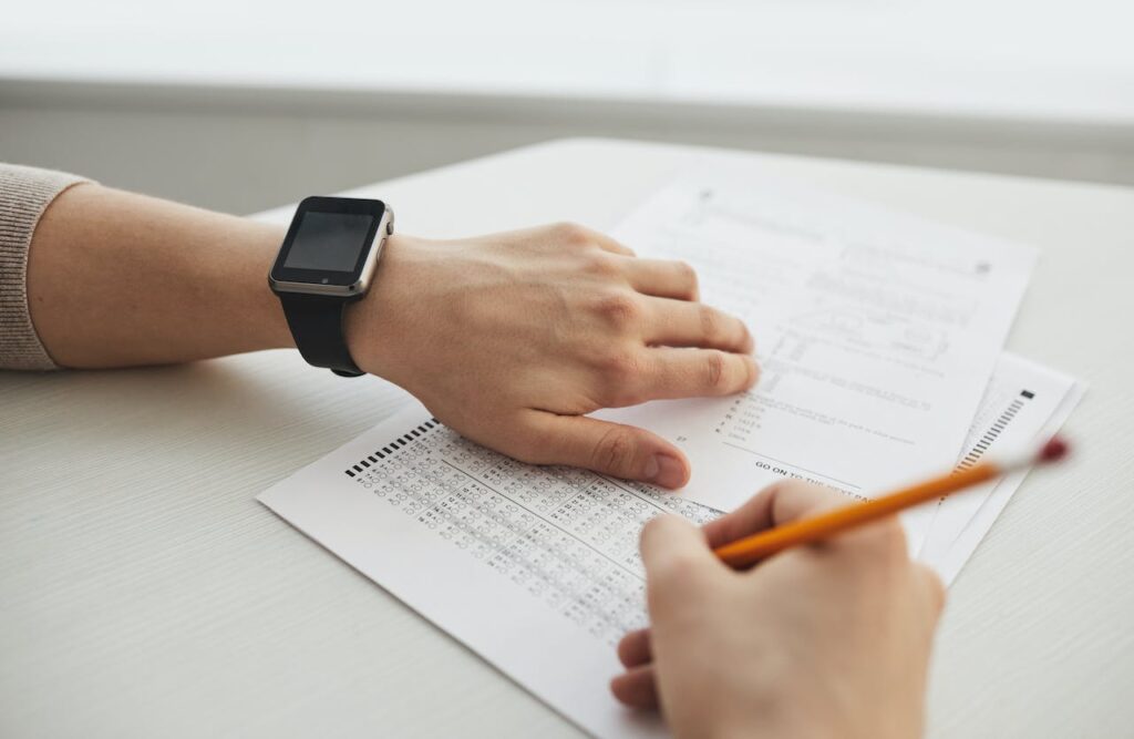 Test cartaceo a crocette. Una mano mantiene il foglio risposte mentre l'altra segna i risultati su un altro foglio con una matita.